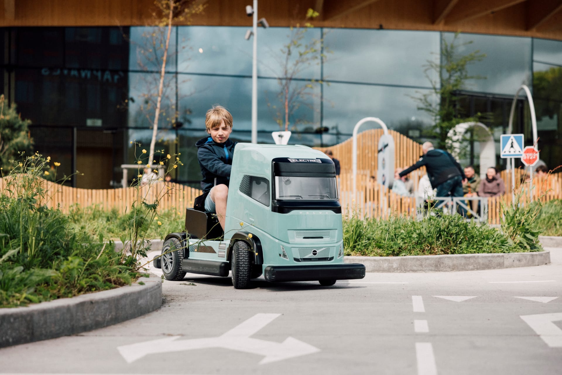 Barn kör eldriven blå Volvo-lastbil i barnstorlek på Traffic School utomhusbana på World of Volvo i Göteborg.